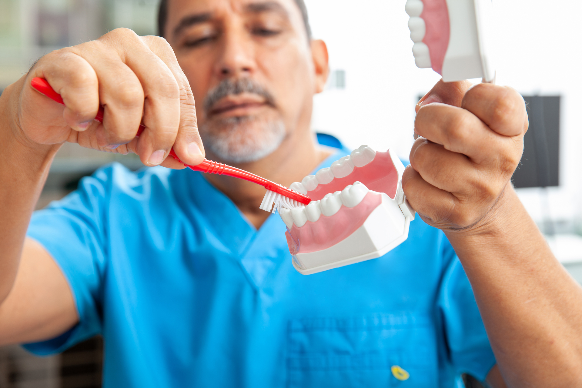 Na tym obrazku możemy zobaczyć dentystę, który dokładnie prezentuje, jak prawidłowo myć zęby. Jest to ważna część edukacji pacjentów na temat higieny jamy ustnej.Dentysta jest profesjonalistą w dziedzinie zdrowia jamy ustnej i jest odpowiedzialny za promowanie prawidłowych praktyk higieny jamy ustnej. Na obrazku widać, że dentysta używa modelu zębów, aby zobrazować technikę szczotkowania zębów